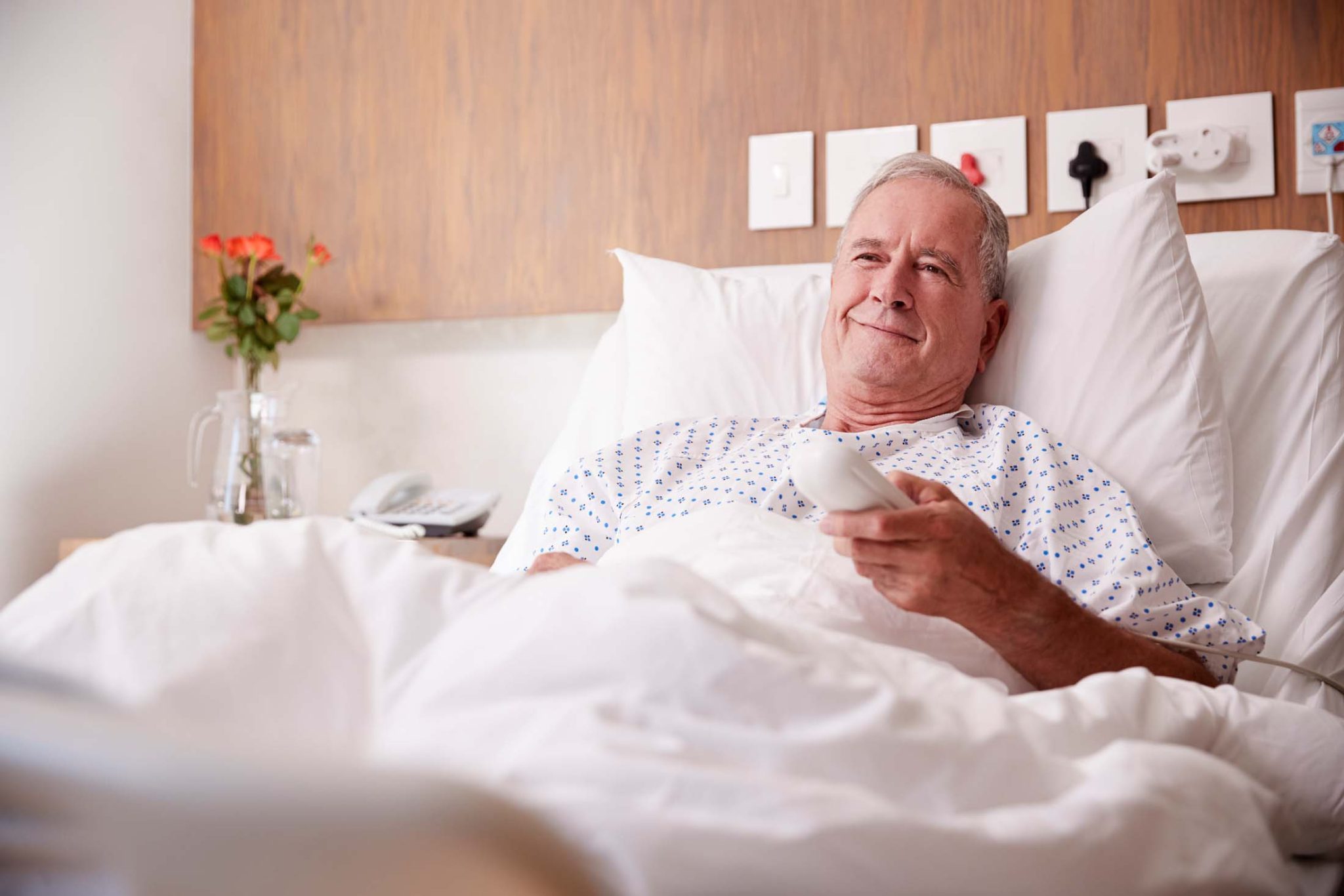 Male Senior Patient Lying In Hospital Bed Watching Television